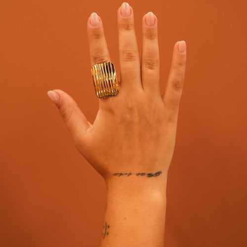 Anel Lifeaskika Crave dourado em aço inoxidável com design texturizado de linhas verticais no dedo de uma mão