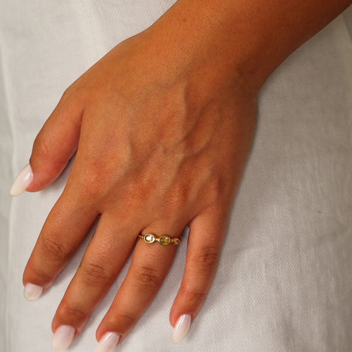 Anel Lifeaskika Dokuji em aço inoxidável dourado com três pedras brancas brilhantes, ajustável no dedo de uma mulher.