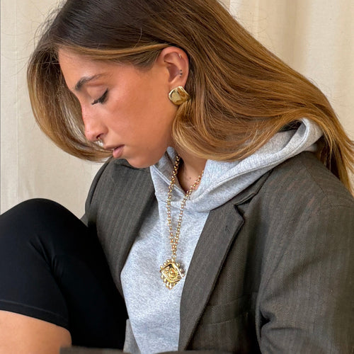 Brincos Lifeaskika Drip em aço inoxidável dourado com design orgânico, usados por modelo com blazer e colar.