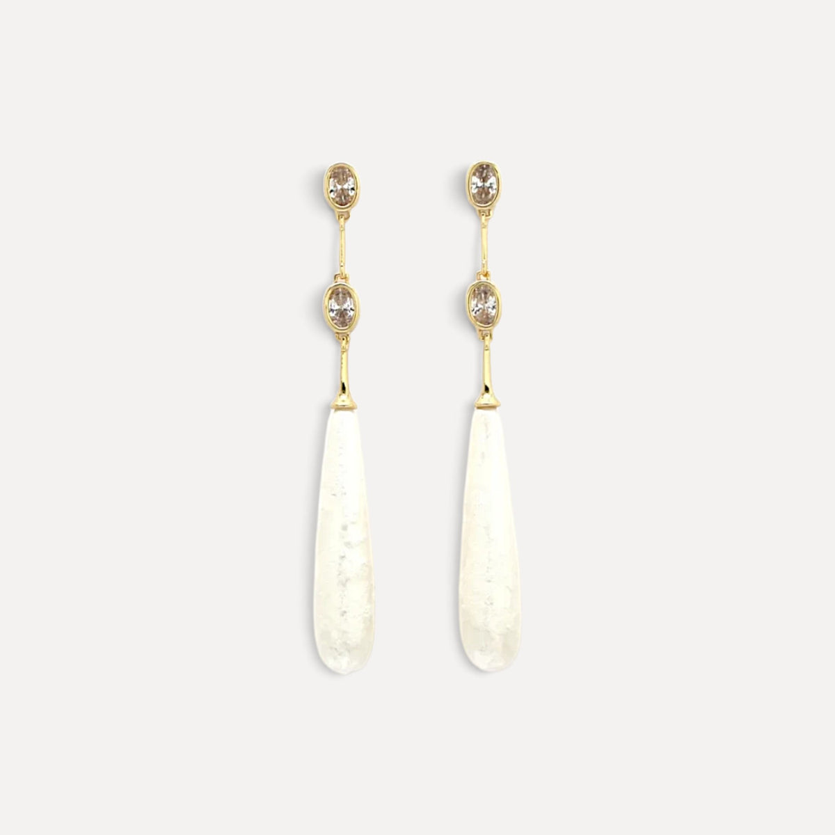 Brincos pendentes Lifeaskika em formato de gota alongada branca com detalhes em strass e estrutura dourada.