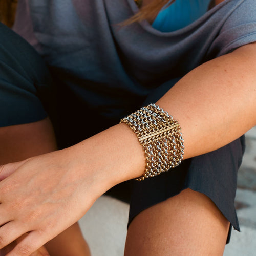 Pulseira Lifeaskika Chōwa larga em aço inoxidável com elos entrelaçados em tons dourado e prateado no pulso feminino